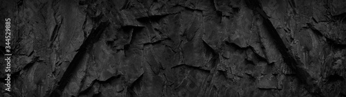 Black and white background. Dark stone grunge background. Mountain texture. Close-up. Wide banner with volumetric rock texture.