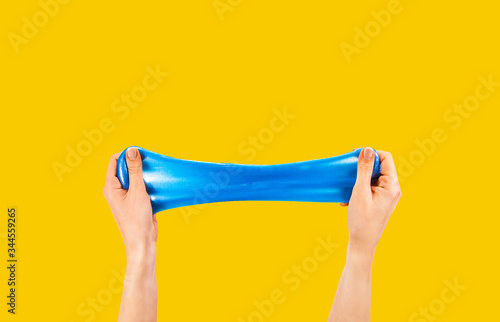 Blue slime stretchable toy for children in hands. An elastic antistress toy for relaxation. Hands gum. Funny Games. Slime on yellow background. Copy space, place for text.