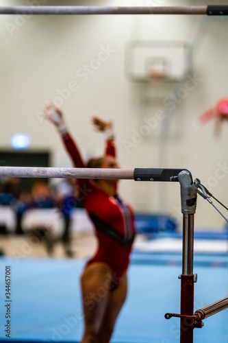 Female gymnast who has just finished her uneven bars routine and is thanking the judges. The woman is out of focus and standing behind the apparatus.
