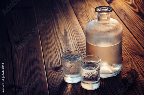 Vodka bottle and two glasses of vodka with ice on a wooden table.