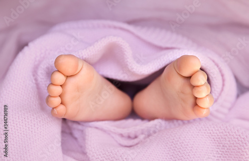 Closeup of baby girl feet wrapped in pastel pink blanket as a background