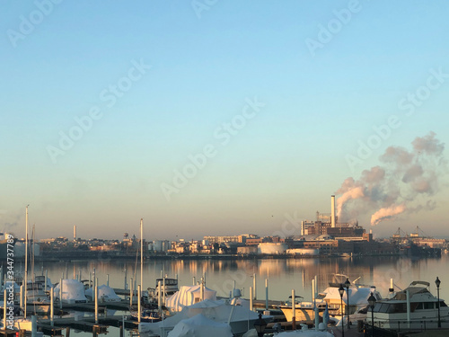 Sunrise over waterfront industrial center with smoke blowing from factory smoke stacks in Baltimore Maryland on Potomac harbor waterfront with yachts in foreground