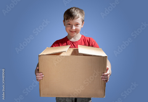 Boy holding a cardboard box on dark background. Donatation. Copy space for text