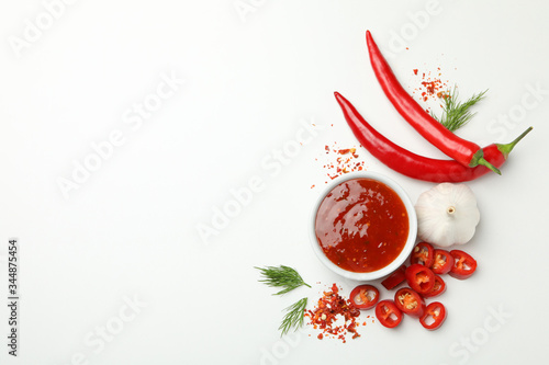 Bowl with chilli sauce, pepper and garlic on white background