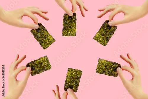 Frame of female hands with crispy seaweed on the pink background with copy space. Dry nori sheets korean or japanese texture. Flat lay. Healthy food concept.