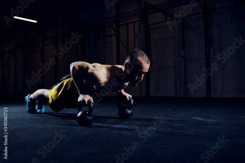 Athletic man exercising kettlebell push-ups at gym
