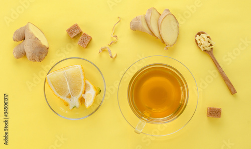 Ginger tea with lemon and spices in glass Cup with spoon and sugar on yellow paper background, top view
