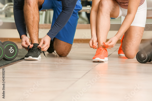 Sporty young couple tying shoelaces in gym in gym