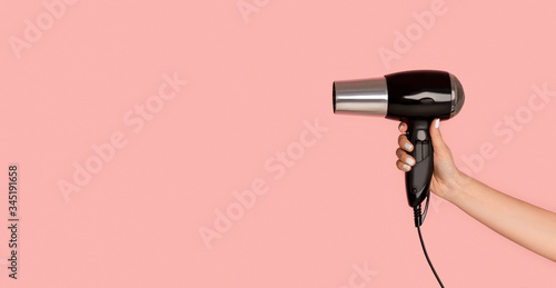 Unrecognizable girl showing hairdryer on pink background, empty space. Panorama