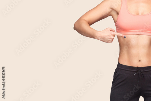 Closeup of fit woman wearing sports tight top and pants pointing herself, showing slim athletic body with trained abdominal muscles, copy space for advertising workouts in gym, weight loss. Healthcare