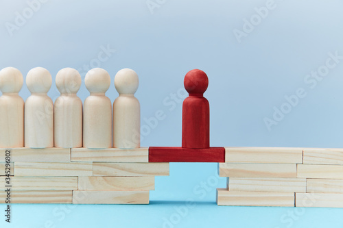 Team leadership mockup. Not like everyone. Risk. Wooden figures in line, one red person miniature ahead on bridge gap