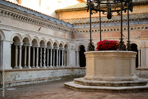 Ancient well with flowers in an abbey cloister in Sassovivo (Italy). Landscape format.