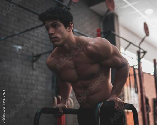 Young, shirtless, muscular athlete doing some dips in parallel bars in the gym. Professional calisthenics athlete working out