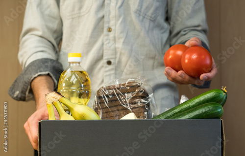 A man puts tomatoes in a donation box. Donations to the needy and the starving during coronavirus. Macaroni, crackers, oil, bread, cucumbers, bananas, tomatoes.