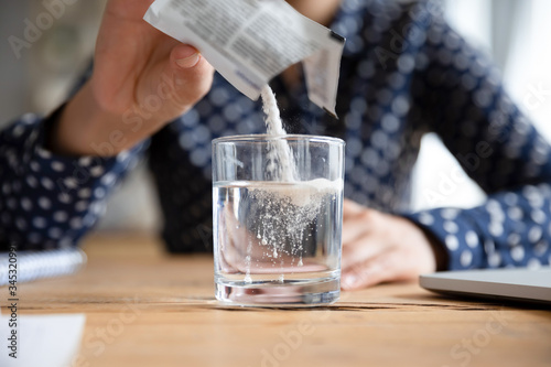 Close up young indian woman pouring soluble anti-influenza powder in glass of water. Sick millennial girl student feeling unwell, relieving grippe fever flu symptoms, high temperature, headache.