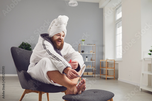Funny pedicure concept. Funny fat man in a bathrobe and a towel paints his nails