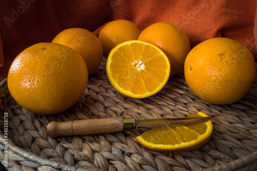 Hermosas naranjas para zumo preparadas con mantel naranja y cuchillo de mango de madera sobre bandeja de ratan.