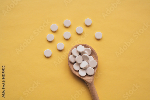 round white tablets on a wooden spoon on a yellow background, tablets are scattered in the center from bottom to top