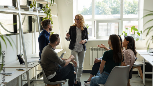 Smiling female leader, coach holding briefing for multiracial team interns in office, teaching students, plan to subordinates. Businesswoman at company meeting with diverse colleagues.