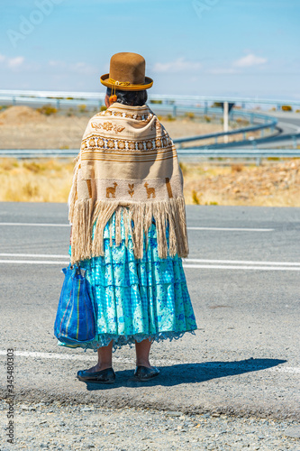 Bolivian indigenous Aymara woman waiting for transport along the highway in traditional clothing, La Paz, Bolivia.