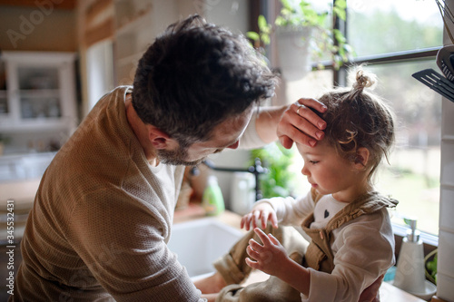 Father checking forehead of sick toddler daughter indoors at home.