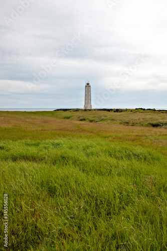 Rocket-shaped lighthouse at the end of a large green meadow with the sea in the background