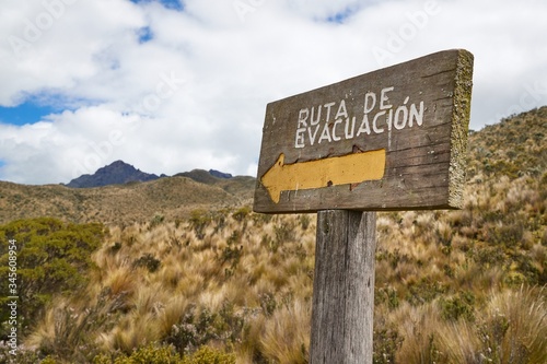 Emergency evacuation route sign in Spanish language at volcano Cotopaxi showing the way to move up to escape pyroclastic flow in case of eruption. The text reads Evacuation route in Spanish.