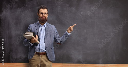 Male teacher holding books and pointing at a chalkboard