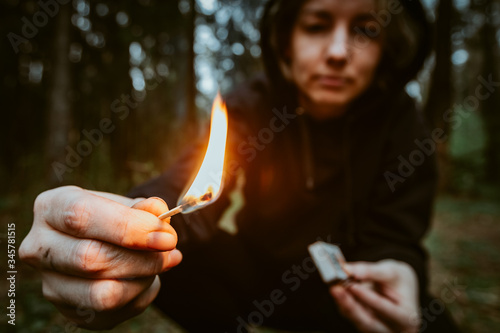 Teenage bully in hood holds burning match in his hand. Forest arsonist. Fire danger. Concept of arson and flame in night