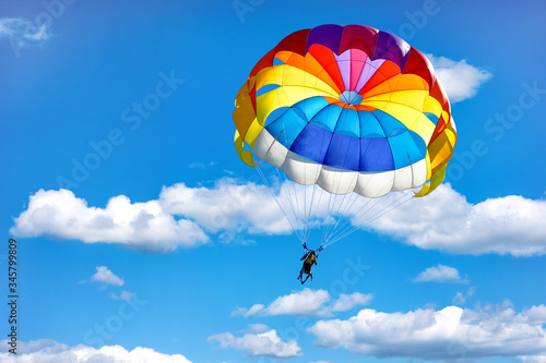 Gliding using a parachute on the background of cloudy blue sky.