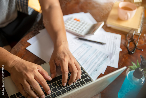 Budget and Tax planning concept. Accountant is calculating company's annual tax and typing laptop. Personal income tax form for who have income under US law place on desk, working on line at home.