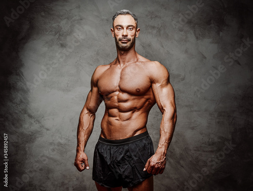 Shirtless adult male bodybuilder posing for a photoshoot shirtless in a dark studio