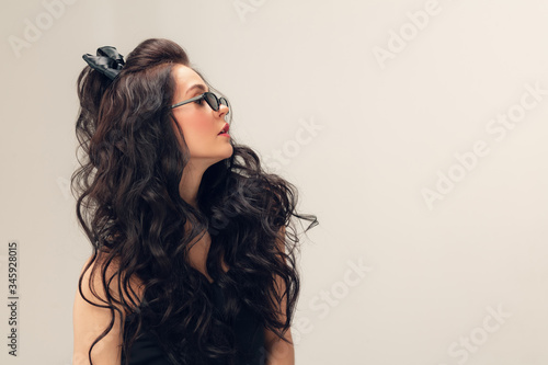 Wearing eyeglasses. Portrait of beautiful young woman on grey studio background. Caucasian cute brunette female model with long curly hair. Concept of beauty, fashion, cosmetics. Copyspace for ad.