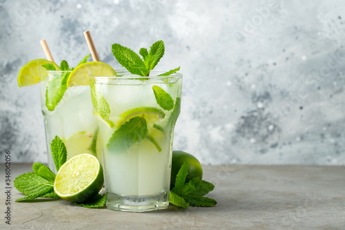 Two homemade lemonade or mojito cocktail with lime, mint and ice cubes in a glass on a light stone table. Fresh summer drink. With copy space.