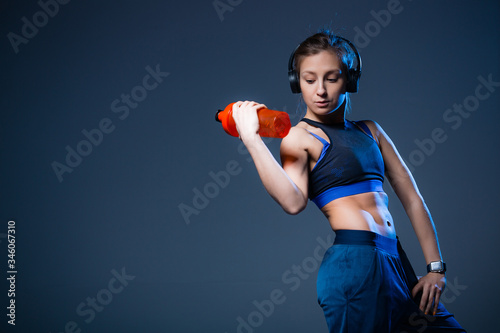 Athlete with a relief pressure of looking for a bottle of water. Girl in headphones and sports blue top.