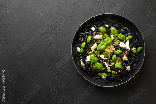 Black pasta spaghetti squid Ink with sauce Pesto in black bowl on black stone background. Top view.