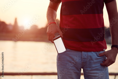 Man holding cellphone in pocket near river.