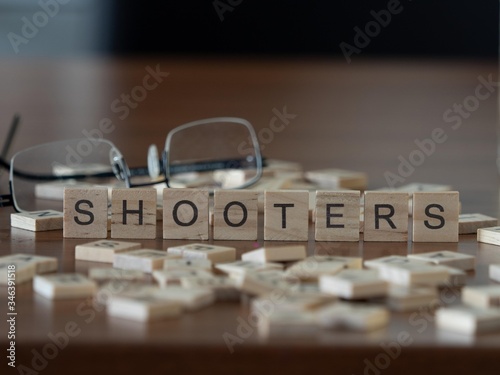 shooters concept represented by wooden letter tiles on a wooden table with glasses and a book