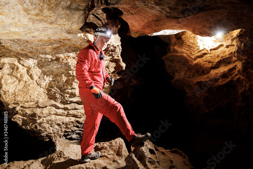 Man walking and exploring dark cave with light headlamp underground. Mysterious deep dark, explorer discovering mystery moody tunnel looking on rock wall inside.