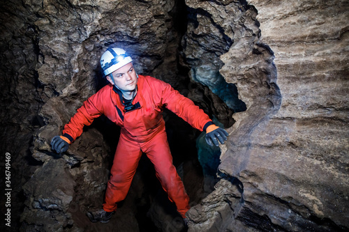 Man walking and exploring dark cave with light headlamp underground. Mysterious deep dark, explorer discovering mystery moody tunnel looking on rock wall inside.