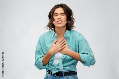 people concept - young woman in turquoise shirt having heartache or heartburn over grey background