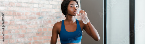 Panoramic orientation of african american sportswoman drinking water in living room