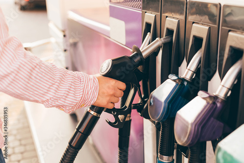 A male hand in striped shirt holding a petrol pump to refuelling a car at gas station