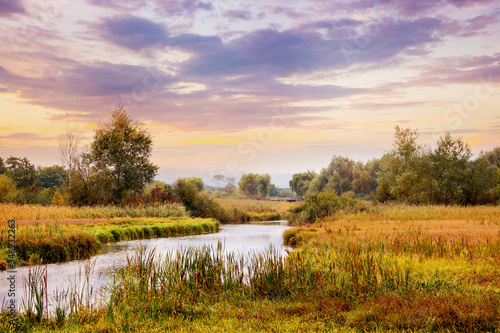 Picturesque autumn landscape with river and cloudy sky at sunset