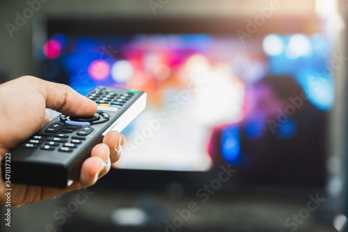 Young man holding television remote control. Hands pointing to tv screen set and turning it on or off select channel watching tv on his sofa at home in the living room relax..