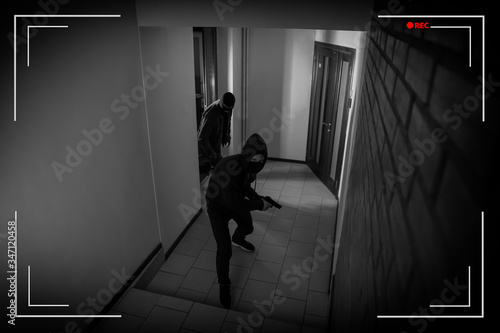 Dangerous criminals in masks with weapon in hallway, view through CCTV camera