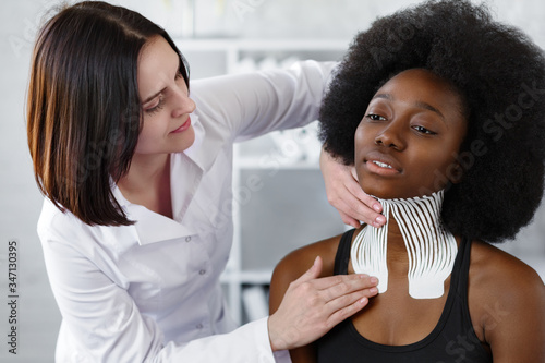 Kinesiology taping. Physiotherapist applying kinesiology tape to patient neck. Therapist treating young female African American athlete. Post traumatic rehabilitation, sport physical therapy.