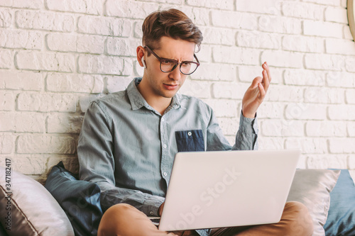 Angry confused businessman freelancer feel irritated while use laptop for work at home. Puzzled impatient hipster man in glasses impressed by bad news from computer. Emotional surprised man on couch