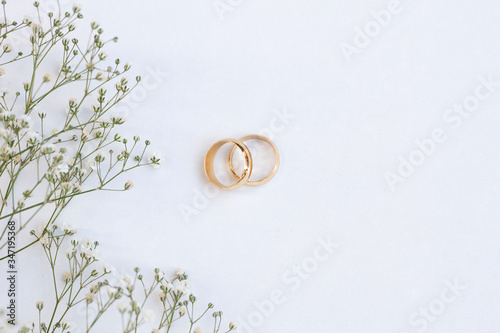 Flowers and two golden wedding rings on white background. Top view.