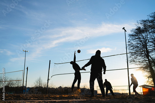 Silhouettes of three men playing beach volleyball,